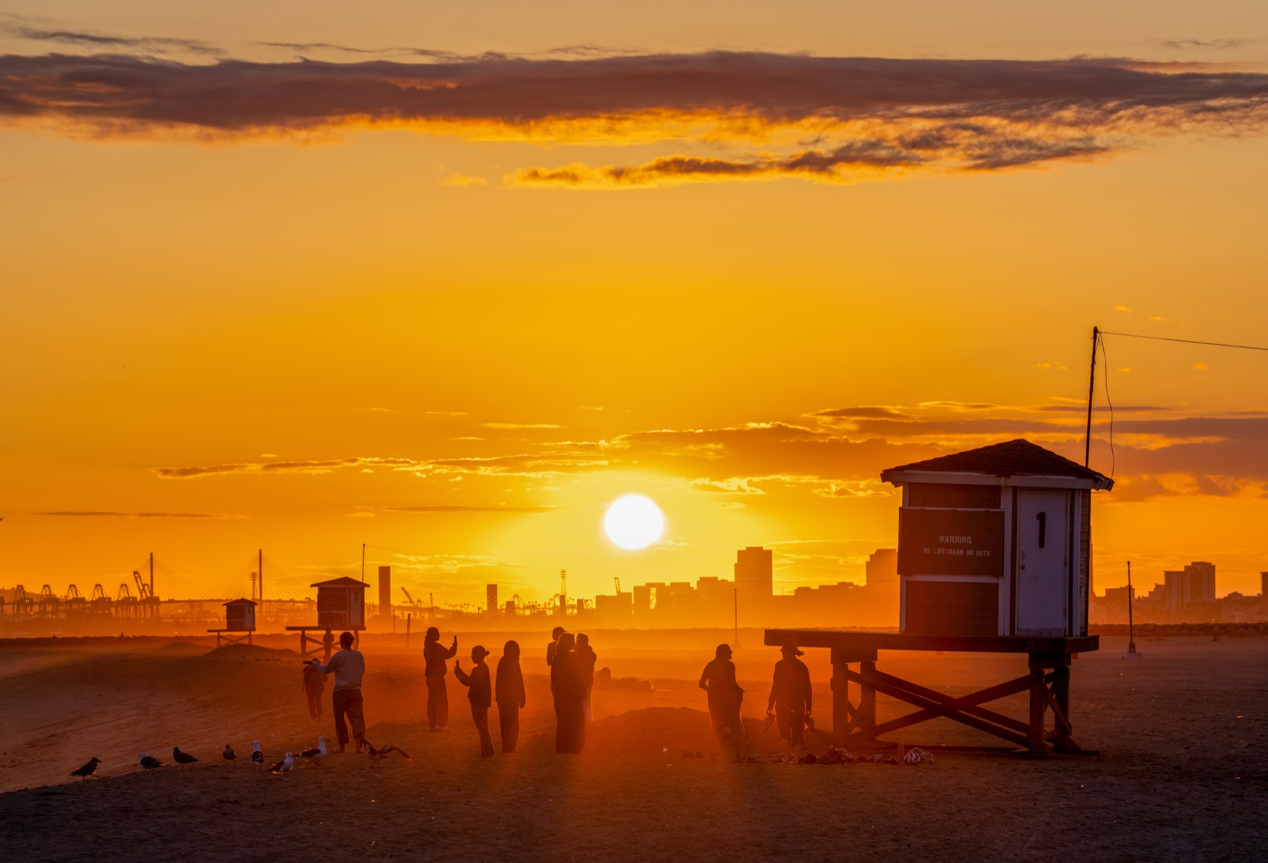 Golden sunset over the Seal Beach coast with people near lifeguard towers