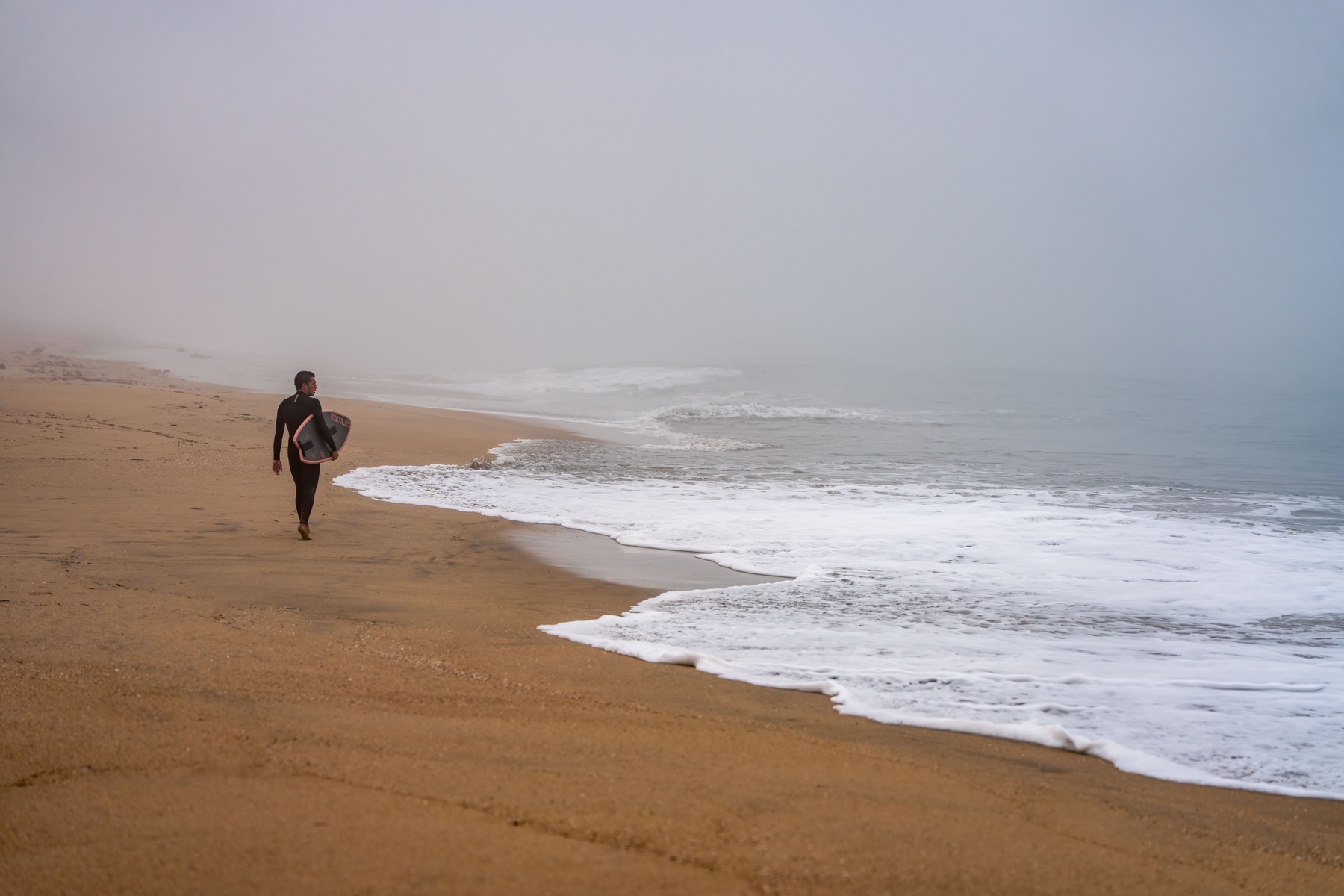 Surfer walking along a foggy Seal Beach shoreline