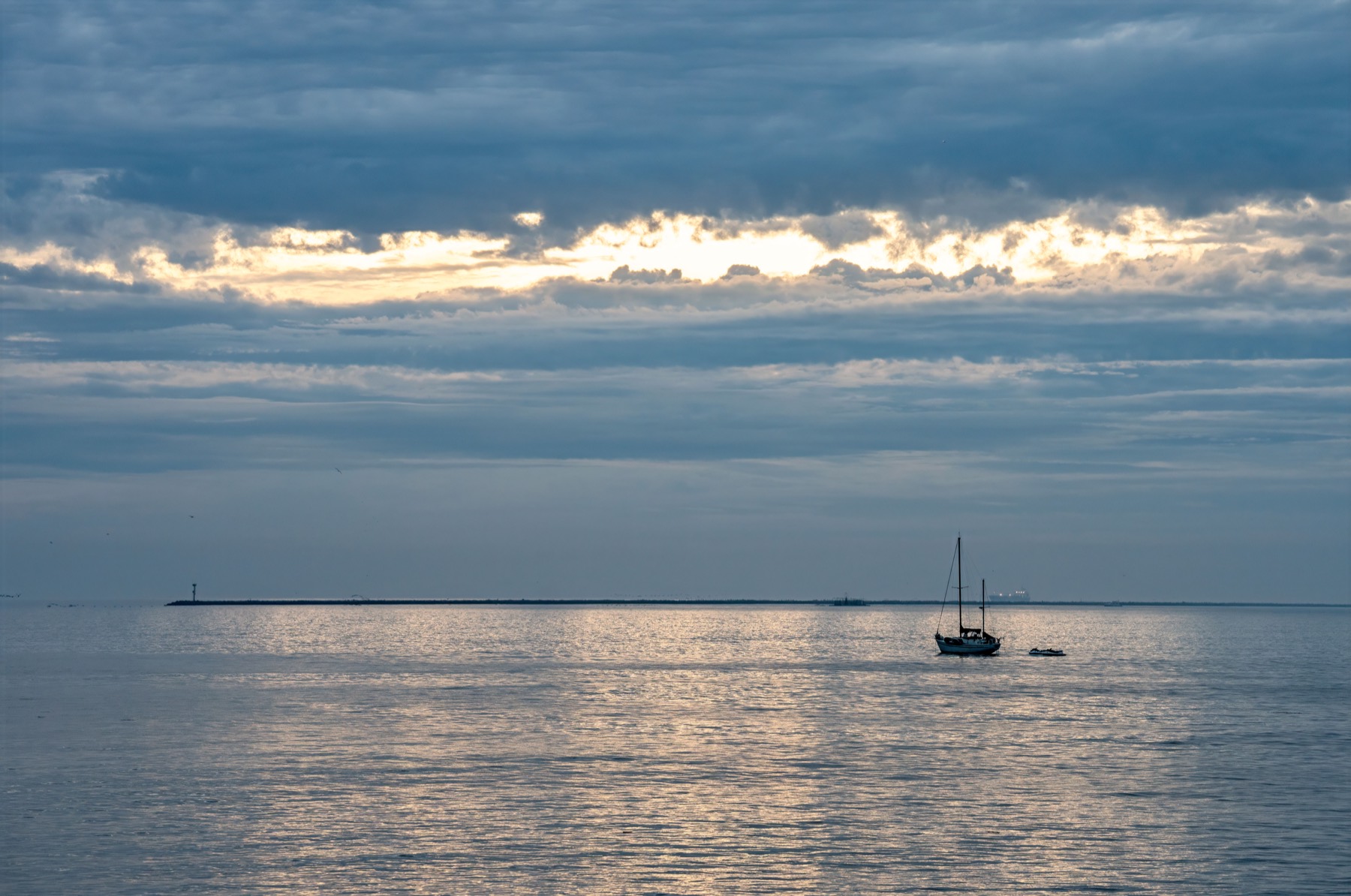 Sailboat on calm water off Seal Beach under dramatic clouds